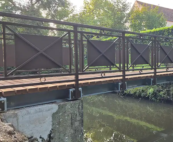 Passerelle piétonne en acier galvanisé et bois installée par SECMI, avec garde-corps latéraux et finitions époxy.
